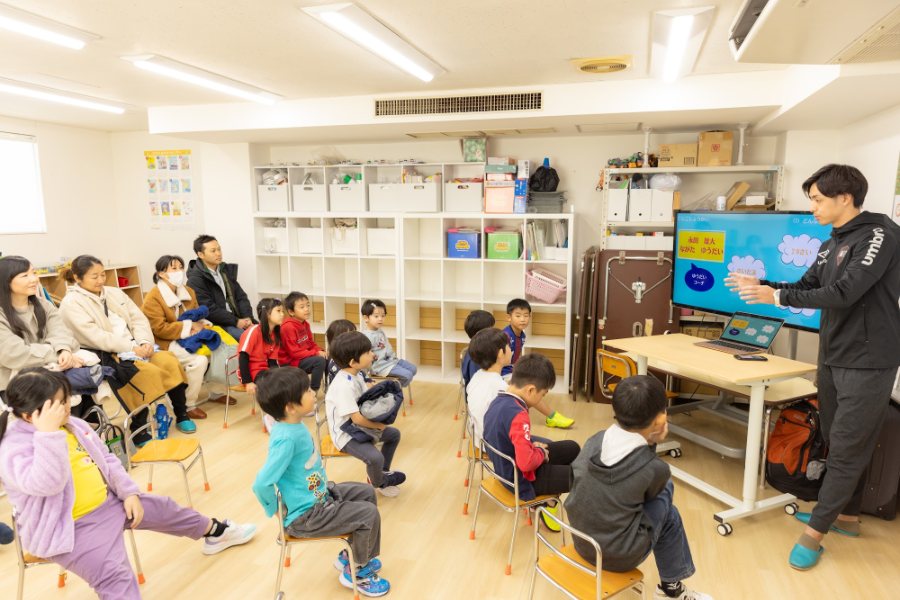 サッカースクールの講演で、子どもたちと保護者にスクリーンを使って話す代表